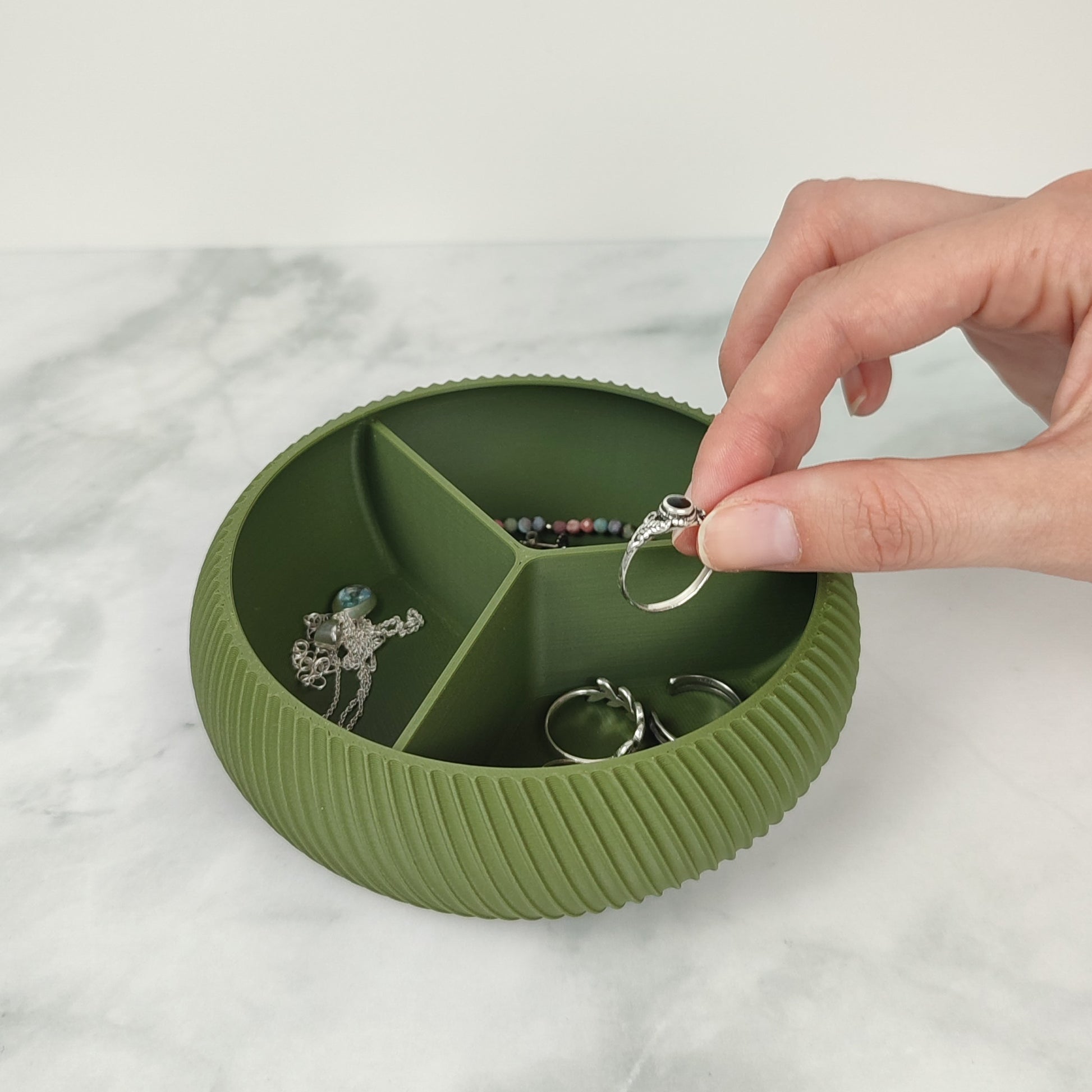 Eine Olive Grüne Schmuckbox mit Fächer, die von Hand mit einem Ring befüllt wird.